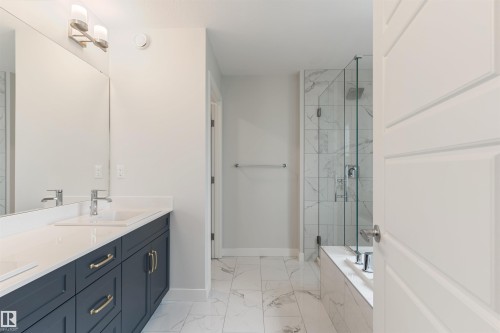 Bathroom featuring a double vanity with dark cabinetry and gold-tone hardware, a large frameless mirror, and a walk-in shower with a glass enclosure and a built-in tub - 6003 Edmonds Place Nw, Edmonton, AB - Indoor Photo Showing Bathroom