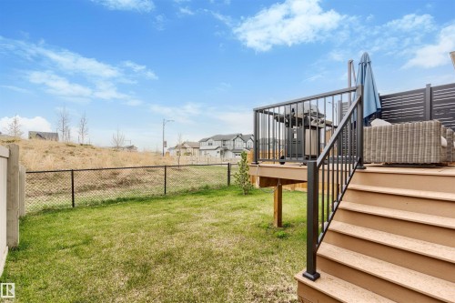 Ground-level backyard featuring green lawn space, a chain-link fence, and a multi-level composite deck with black metal railings - 6003 Edmonds Place Nw, Edmonton, AB - Outdoor