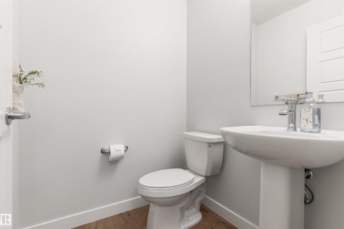 Pedestal sink with chrome faucet, a white toilet, wood-finish flooring, and a wall-mounted mirror - 6003 Edmonds Place Nw, Edmonton, AB - Indoor Photo Showing Bathroom