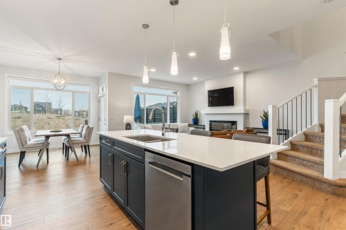 Kitchen island with a white countertop and dark cabinetry featuring a built-in sink and stainless steel dishwasher - 6003 Edmonds Place Nw, Edmonton, AB - Indoor Photo Showing Kitchen With Fireplace With Double Sink With Upgraded Kitchen