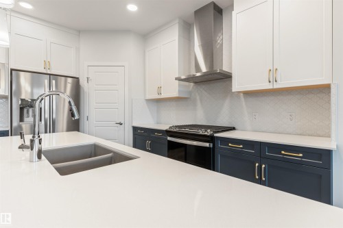 Kitchen featuring a central island with an undermount dual-basin sink, quartz countertops, stainless steel appliances, and two-tone cabinetry with gold-tone hardware - 6003 Edmonds Place Nw, Edmonton, AB - Indoor Photo Showing Kitchen With Double Sink With Upgraded Kitchen