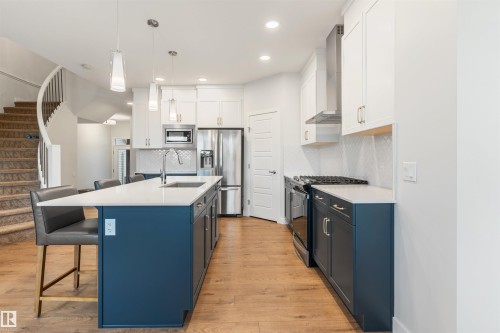 Contemporary kitchen featuring a large island with white countertop, stainless steel appliances, white upper cabinetry, and contrasting blue lower cabinetry - 6003 Edmonds Place Nw, Edmonton, AB - Indoor Photo Showing Kitchen With Upgraded Kitchen