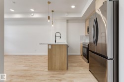 Modern kitchen featuring an island with a light-toned wood finish, a matte black faucet, and pendant lighting - 