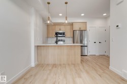 Modern kitchen featuring light wood-finish cabinetry, stainless steel appliances, a white countertop island, and wood-finish flooring - 
