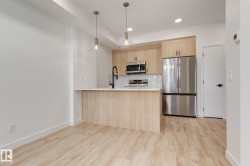 Modern kitchen with light wood-finish cabinetry, stainless steel appliances, and a central island with a light-toned countertop - 