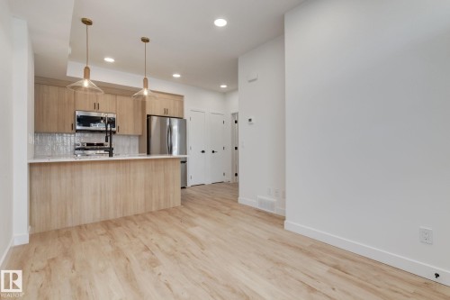 Kitchen featuring wood-finish cabinetry, stainless steel appliances, a white subway tile backsplash, a countertop island, and pendant lighting - 16231 19 Avenue, Edmonton, AB - Indoor Photo Showing Kitchen