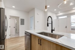 Kitchen island featuring a stainless steel undermount sink with a matte black pull-down faucet, light wood-finish cabinetry, and a white countertop with subtle veining - 