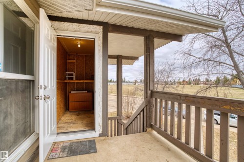Covered entryway with concrete flooring, wood-finish railings, and a built-in storage closet featuring shelves and an overhead light - 1116 Saddleback Road, Edmonton, AB - Outdoor With Exterior
