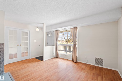 Bright living area featuring wood-finish flooring, a large window with white trim, and a partial brick fireplace surround - 1116 Saddleback Road, Edmonton, AB - Indoor