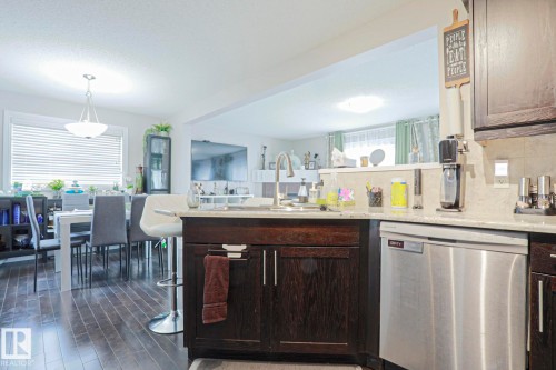 Kitchen featuring dark wood-finish cabinetry, light stone countertops, stainless steel dishwasher, and a tile backsplash - 1621 64 Street, Edmonton, AB - Indoor Photo Showing Kitchen
