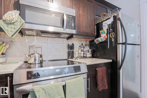 Kitchen featuring dark wood cabinetry, light-toned countertops, tile backsplash, stainless steel microwave, and integrated electric cooktop - 1621 64 Street, Edmonton, AB - Indoor Photo Showing Kitchen