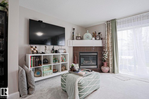 Living space featuring a tile-surround fireplace with mantel, soft carpeting, a multi-pane glass door, and a built-in shelving unit - 1621 64 Street, Edmonton, AB - Indoor Photo Showing Living Room With Fireplace