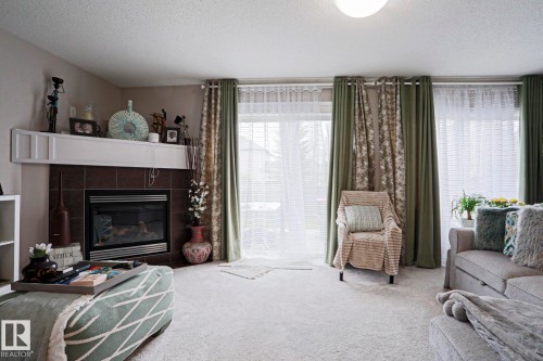 Living area featuring light-colored carpeting and a tiled fireplace with a white mantel - 1621 64 Street, Edmonton, AB - Indoor Photo Showing Living Room With Fireplace