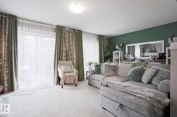 Bright living area featuring a full wall of windows with blinds and drapes, a green accent wall, and light-toned carpeting - 