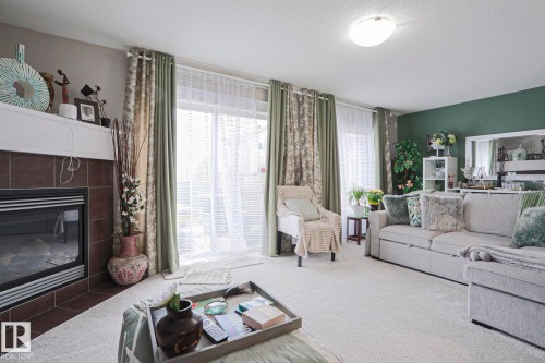 Living area featuring a fireplace with a tiled surround and white mantel, a sliding glass door with sheer and patterned drapes, a large light-toned sectional sofa, and light-colored carpeting throughout - 1621 64 Street, Edmonton, AB - Indoor Photo Showing Living Room With Fireplace