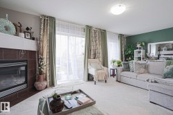 Living area featuring a fireplace with a tiled surround and white mantel, a sliding glass door with sheer and patterned drapes, a large light-toned sectional sofa, and light-colored carpeting throughout - 