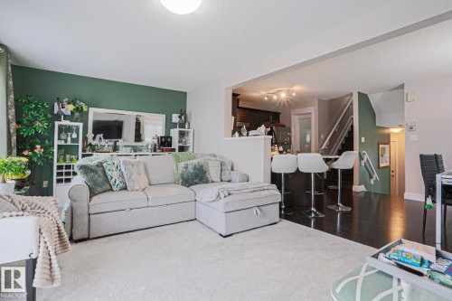 Open-concept living area featuring light-toned carpeting, a partial green accent wall, recessed lighting, and an adjacent kitchen space with dark wood-finish flooring and track lighting - 1621 64 Street, Edmonton, AB - Indoor Photo Showing Living Room