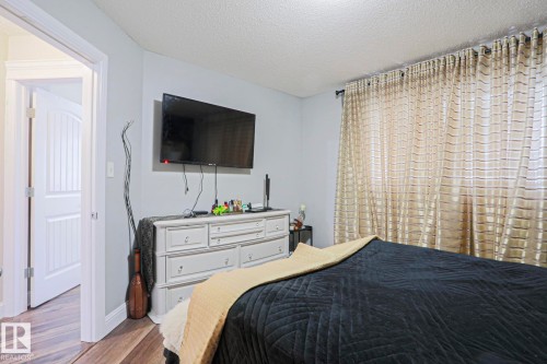 Spacious interior room featuring wood-finish flooring, a wall-mounted flat-screen display, and patterned floor-to-ceiling drapery - 1621 64 Street, Edmonton, AB - Indoor Photo Showing Bedroom
