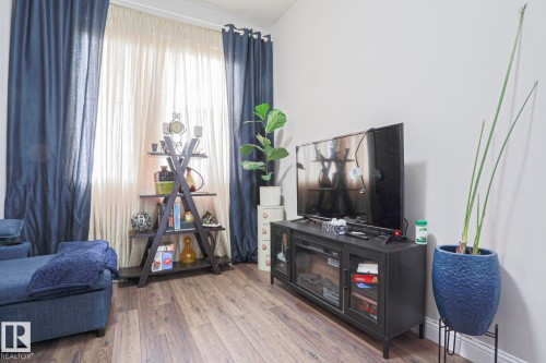 Spacious interior featuring wood-finish flooring, light-toned walls, and a large window with privacy sheers and opaque drapery panels - 1621 64 Street, Edmonton, AB - Indoor With Fireplace