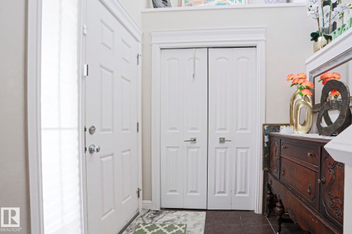 Entryway featuring a white paneled front door with a full-length sidelight, a bi-fold closet with matching hardware, crown molding, and dark tile flooring - 1621 64 Street, Edmonton, AB - Indoor Photo Showing Other Room