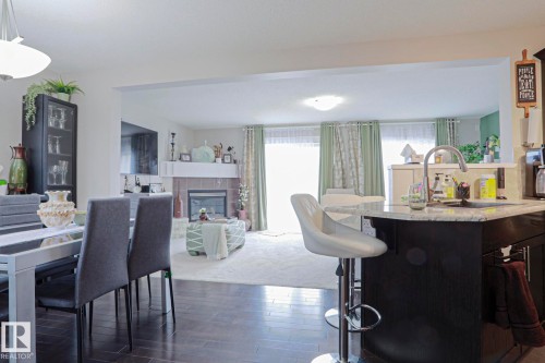 Spacious dining area with dark wood-finish flooring, featuring a kitchen island with a light-colored countertop and a built-in sink - 1621 64 Street, Edmonton, AB - Indoor Photo Showing Dining Room With Fireplace