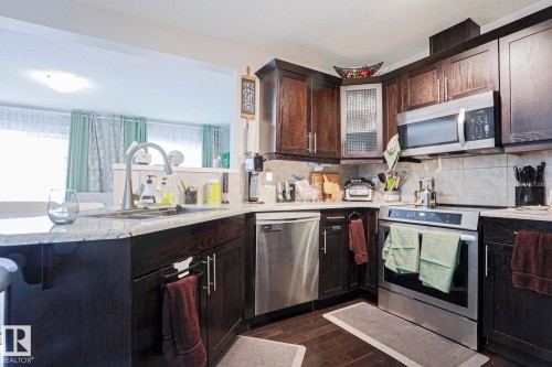 Kitchen featuring dark wood-finish cabinetry, stainless steel appliances, granite countertops, and a tile backsplash - 1621 64 Street, Edmonton, AB - Indoor Photo Showing Kitchen With Double Sink