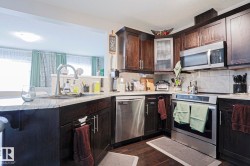 Kitchen featuring dark wood-finish cabinetry, stainless steel appliances, granite countertops, and a tile backsplash - 
