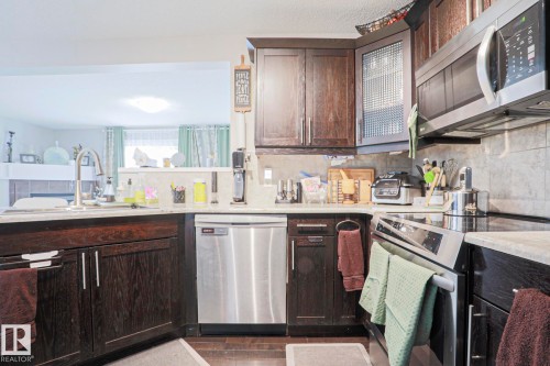 Kitchen featuring dark wood-finish cabinetry, stainless steel appliances, a tile backsplash, and light-toned countertops - 1621 64 Street, Edmonton, AB - Indoor Photo Showing Kitchen With Stainless Steel Kitchen With Double Sink