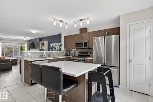 Contemporary kitchen featuring wood-finish cabinetry, stainless steel appliances, and a white countertop island - 16 7503 Getty Gate, Edmonton, AB - Indoor Photo Showing Kitchen With Stainless Steel Kitchen With Upgraded Kitchen