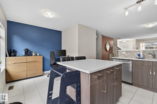 Open-concept kitchen featuring an island with a light-toned countertop, wood-finish cabinetry, and stainless steel appliances - 16 7503 Getty Gate, Edmonton, AB - Indoor Photo Showing Kitchen