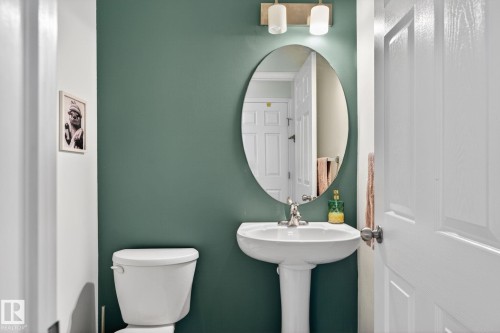 Pedestal sink with chrome faucet, oval mirror, and wall-mounted light fixture - 16 7503 Getty Gate, Edmonton, AB - Indoor Photo Showing Bathroom