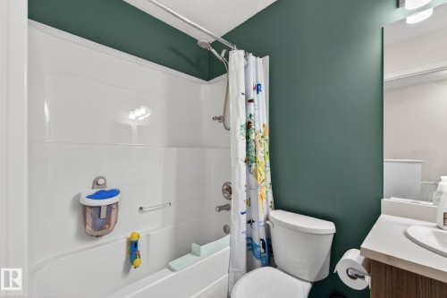 Full bathroom featuring a white tub/shower combination, white toilet, and a vanity with a light-toned countertop and wood-finish cabinetry - 16 7503 Getty Gate, Edmonton, AB - Indoor Photo Showing Bathroom