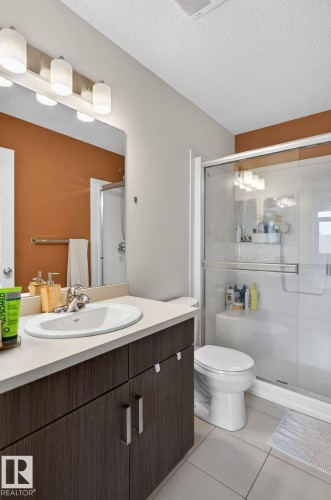 Modern bathroom featuring a single vanity with a wood-finish cabinet, integrated sink, and light-toned countertop - 16 7503 Getty Gate, Edmonton, AB - Indoor Photo Showing Bathroom