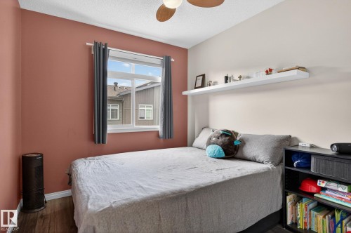 Bedroom featuring wood-finish flooring, a contemporary ceiling fan, and a window with dark curtains - 16 7503 Getty Gate, Edmonton, AB - Indoor Photo Showing Bedroom
