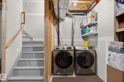 Dedicated laundry area featuring two front-loading machines, overhead exposed ductwork, and built-in shelving - 16 7503 Getty Gate, Edmonton, AB - Indoor Photo Showing Laundry Room