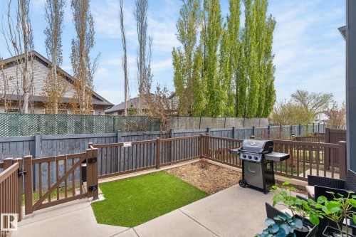 Concrete patio area featuring a section of artificial turf and a brown picket fence with a gate - 16 7503 Getty Gate, Edmonton, AB - Outdoor