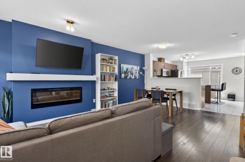 Living area featuring dark wood-finish flooring and a blue accent wall with an integrated linear fireplace - 16 7503 Getty Gate, Edmonton, AB - Indoor Photo Showing Living Room With Fireplace