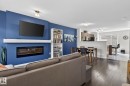 Living area featuring dark wood-finish flooring and a blue accent wall with an integrated linear fireplace - 16 7503 Getty Gate, Edmonton, AB  - Indoor Photo Showing Living Room With Fireplace 