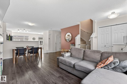 Open-concept living space featuring wood-finish flooring, a contemporary staircase with white risers, and a built-in shelving unit - 16 7503 Getty Gate, Edmonton, AB - Indoor Photo Showing Living Room