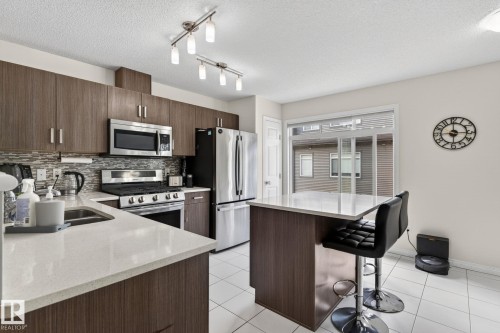 Modern kitchen featuring wood-finish cabinetry, stainless steel appliances, light-toned countertops, and white tile flooring - 16 7503 Getty Gate, Edmonton, AB - Indoor Photo Showing Kitchen With Stainless Steel Kitchen With Double Sink With Upgraded Kitchen