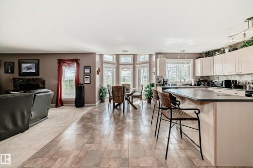 Open-concept interior featuring wood-finish flooring, a kitchen island with seating, ample cabinetry, and a dining area with a bay window - 5107 200 Street, Edmonton, AB - Indoor