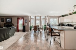 Open-concept interior featuring wood-finish flooring, a kitchen island with seating, ample cabinetry, and a dining area with a bay window - 