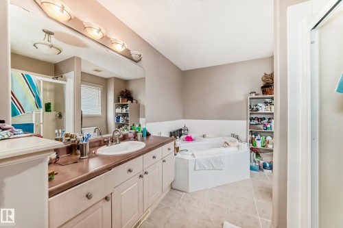 Bathroom featuring a built-in corner soaking tub, a single vanity with an integrated sink, a large wall mirror, and a standing shower enclosure - 5107 200 Street, Edmonton, AB - Indoor Photo Showing Bathroom