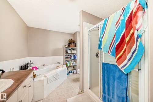 Bathroom featuring a glass-enclosed shower, a built-in corner bathtub, and a vanity with a white basin sink and dark wood-finish countertop - 5107 200 Street, Edmonton, AB - Indoor Photo Showing Bathroom
