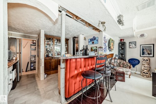Custom wet bar featuring upholstered red paneling and three bar stools - 5107 200 Street, Edmonton, AB - Indoor