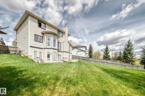 Rear exterior featuring light-colored siding with dark trim, a bay window on the main level, and multiple glass-paned doors providing direct yard access - 5107 200 Street, Edmonton, AB - Outdoor