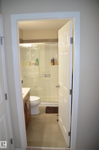 Compact bathroom featuring a glass-enclosed shower, wood-finish vanity with countertop, and tile flooring - 1412 152, Edmonton, AB - Indoor Photo Showing Bathroom