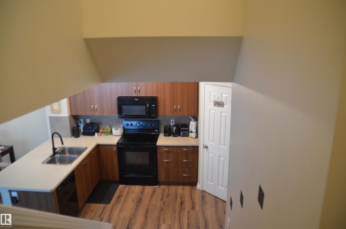 U-shaped kitchen featuring wood-finish cabinetry, light-toned countertops, and wood-look flooring - 1412 152, Edmonton, AB - Indoor Photo Showing Kitchen With Double Sink