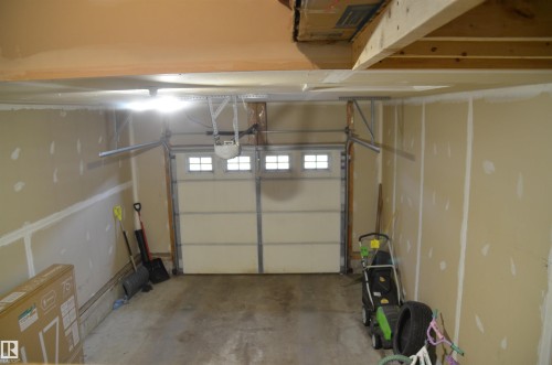 Spacious garage featuring a paneled overhead door with upper window lights, an automatic opener, and exposed ceiling joists - 1412 152, Edmonton, AB - Indoor Photo Showing Garage