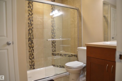 Glass-enclosed shower with tile surround and decorative mosaic accents - 1412 152, Edmonton, AB - Indoor Photo Showing Bathroom